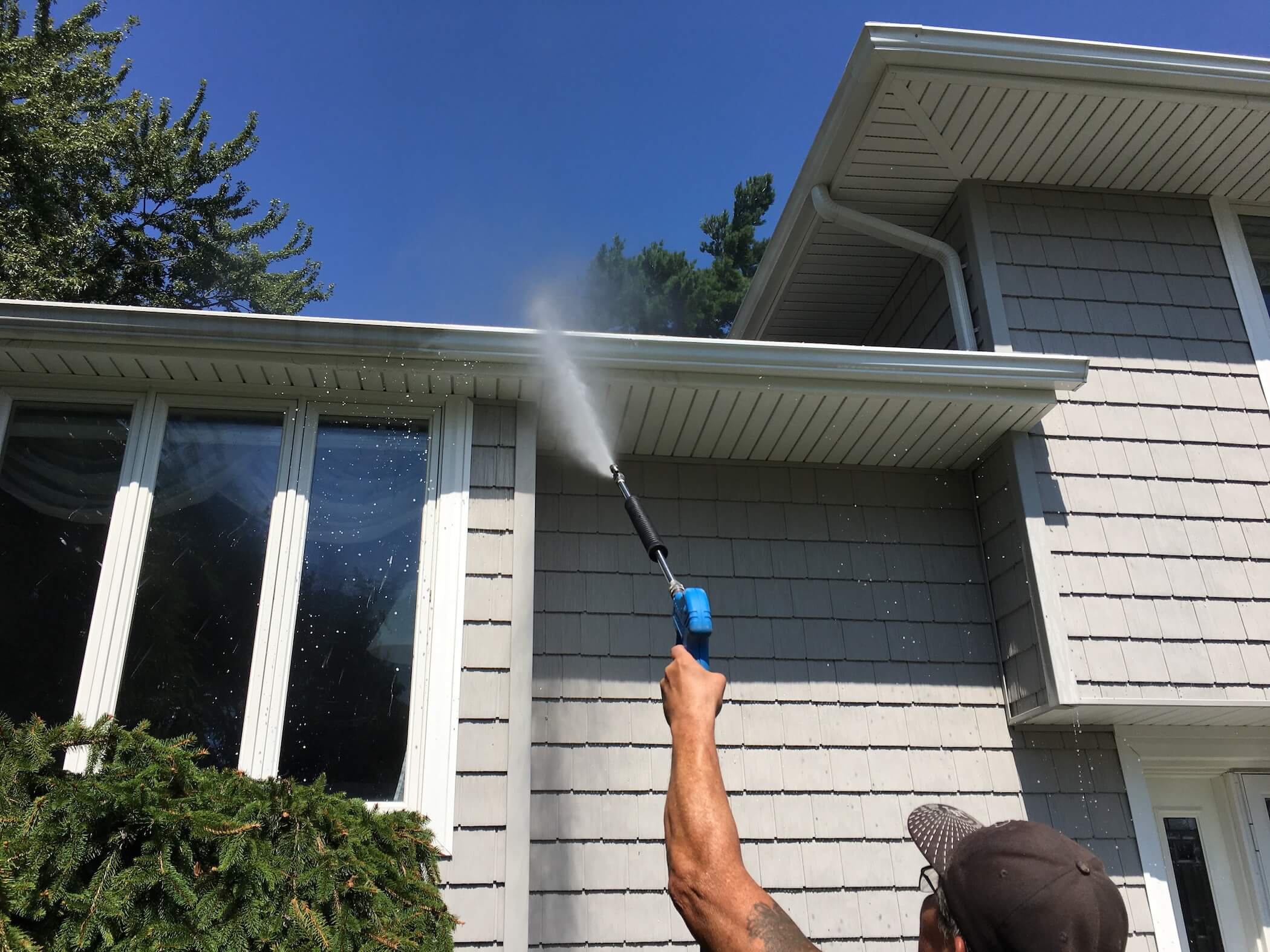 Technician carefully cleaning vinyl siding with low-pressure house washing equipment