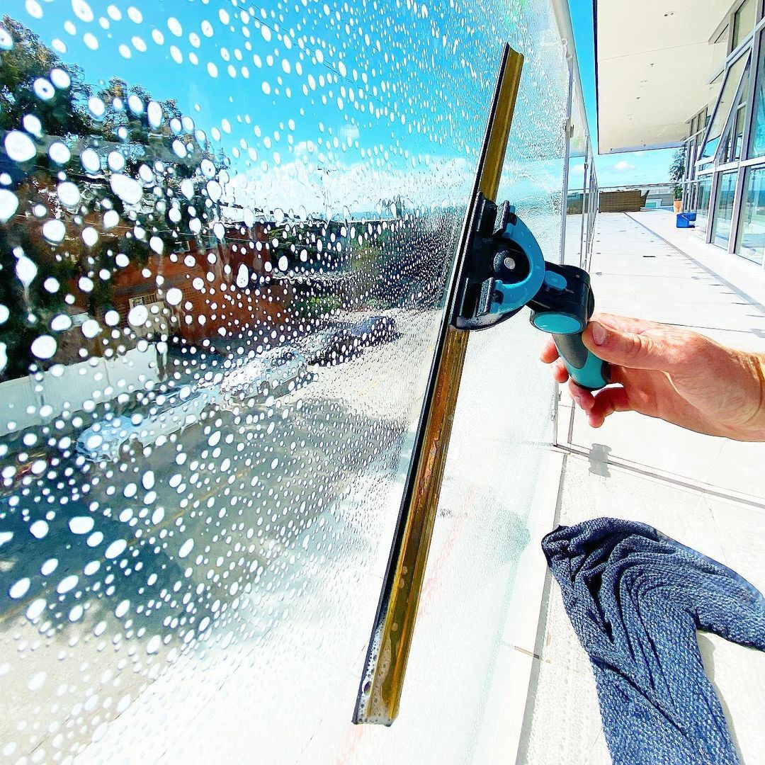 Experienced cleaner removing water spots from exterior glass with professional window tools