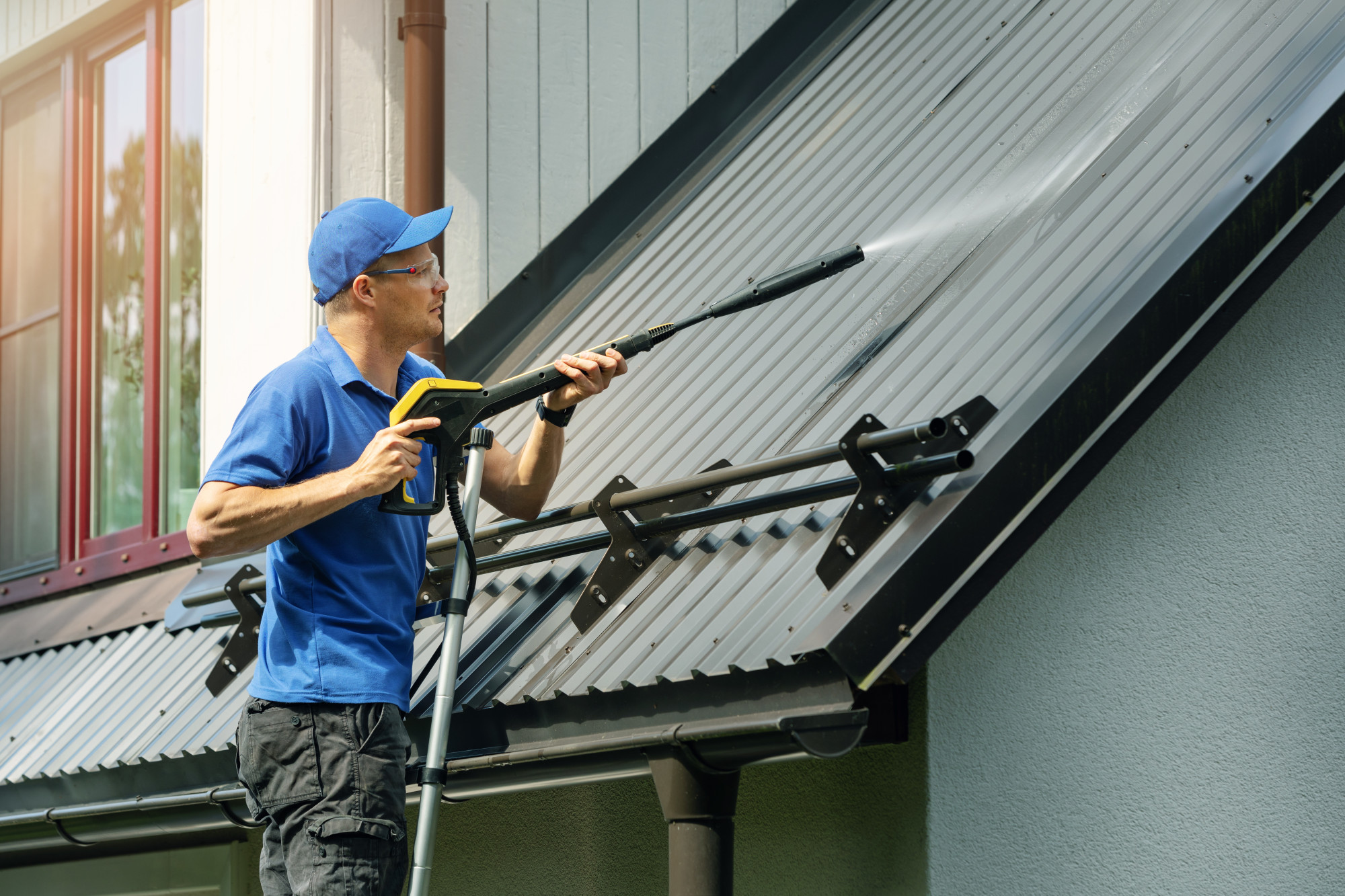 Technician cleaning black roof streaks from asphalt shingles on a residential home
